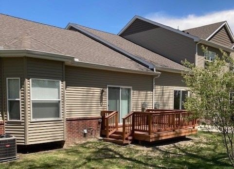 rear view of house with central AC unit, a yard, a deck, and a shingled roof