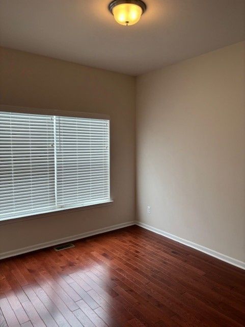 spare room with baseboards, dark wood-style flooring, and visible vents