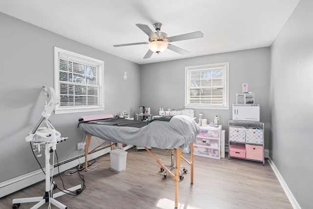 interior space featuring a ceiling fan, baseboards, a baseboard heating unit, and wood finished floors