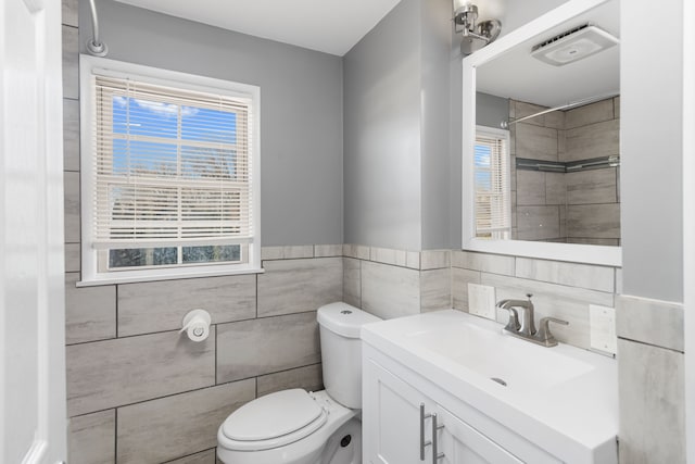 bathroom with wainscoting, vanity, toilet, tile walls, and visible vents