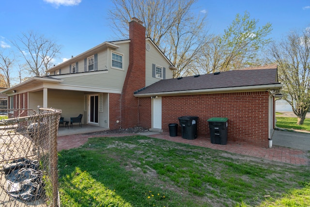 rear view of house featuring roof with shingles, brick siding, a chimney, a patio area, and a yard