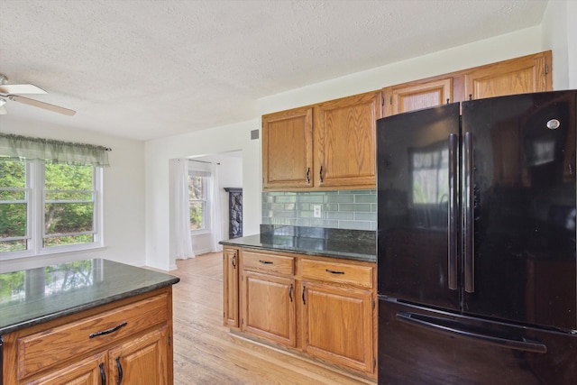 kitchen with a ceiling fan, a textured ceiling, brown cabinets, freestanding refrigerator, and light wood-style flooring