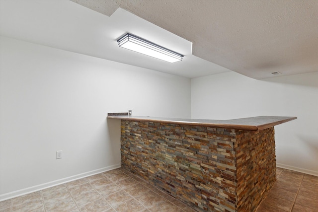 bar featuring a bar, a textured ceiling, baseboards, and tile patterned floors