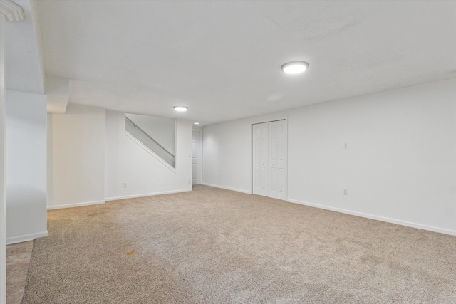 finished basement featuring light colored carpet, baseboards, and stairway