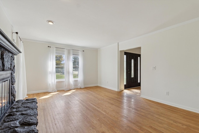 unfurnished living room with crown molding, baseboards, light wood-type flooring, and a stone fireplace