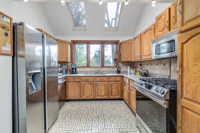 kitchen with appliances with stainless steel finishes, a sink, vaulted ceiling with skylight, brick patterned floor, and backsplash