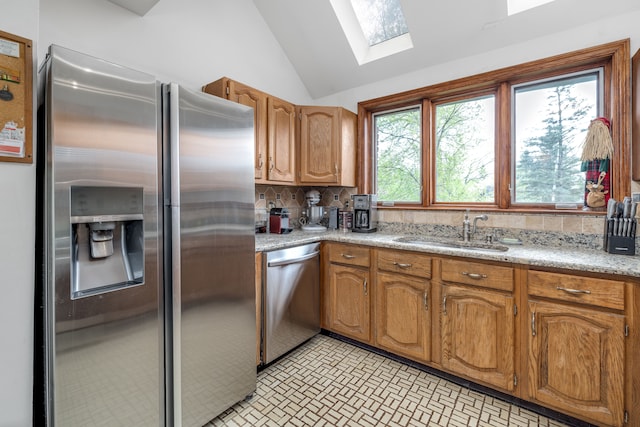 kitchen with brown cabinetry, lofted ceiling with skylight, tasteful backsplash, a sink, and appliances with stainless steel finishes