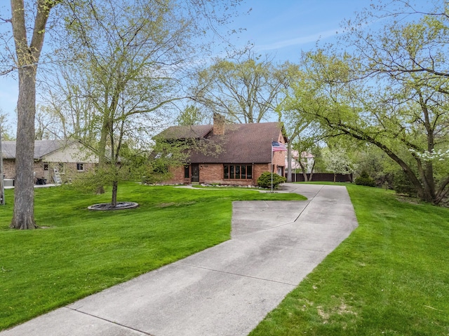 view of front of property featuring a front lawn, roof with shingles, a chimney, brick siding, and driveway