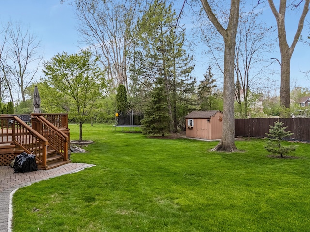 view of yard featuring a trampoline, a deck, an outbuilding, fence, and a storage unit