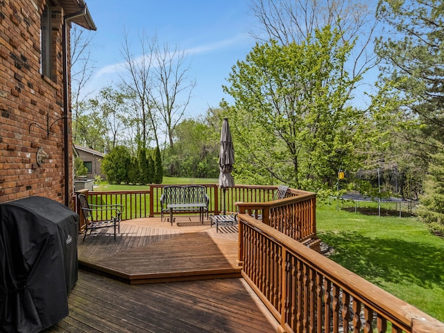deck featuring a lawn, a trampoline, and a grill