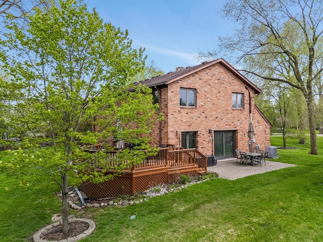 back of property with a lawn, a wooden deck, a patio area, brick siding, and central AC