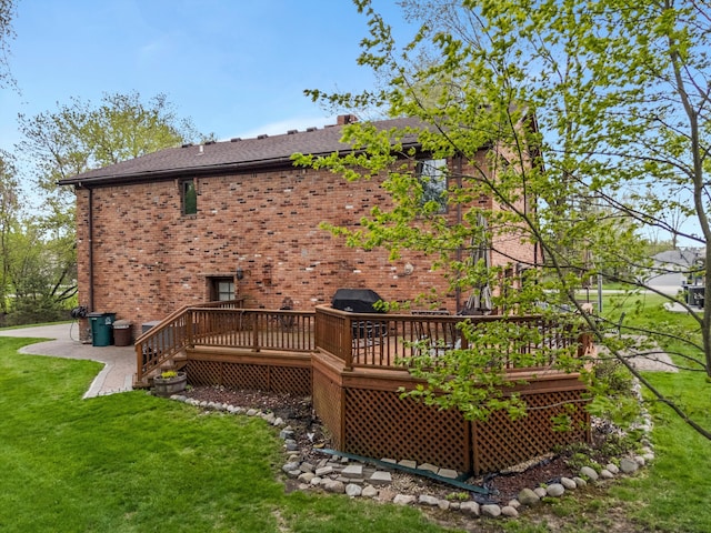 rear view of house featuring a lawn, brick siding, roof with shingles, and a deck
