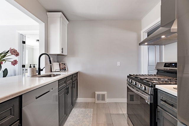 kitchen featuring visible vents, wall chimney range hood, light countertops, a sink, and appliances with stainless steel finishes