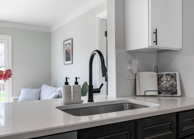 kitchen with dark cabinets, a sink, light stone counters, and a healthy amount of sunlight