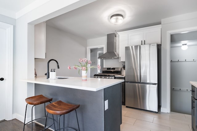 kitchen featuring wall chimney range hood, appliances with stainless steel finishes, a sink, light countertops, and a kitchen breakfast bar