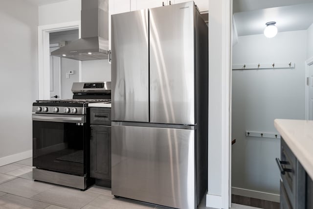 kitchen featuring light countertops, appliances with stainless steel finishes, baseboards, and wall chimney exhaust hood
