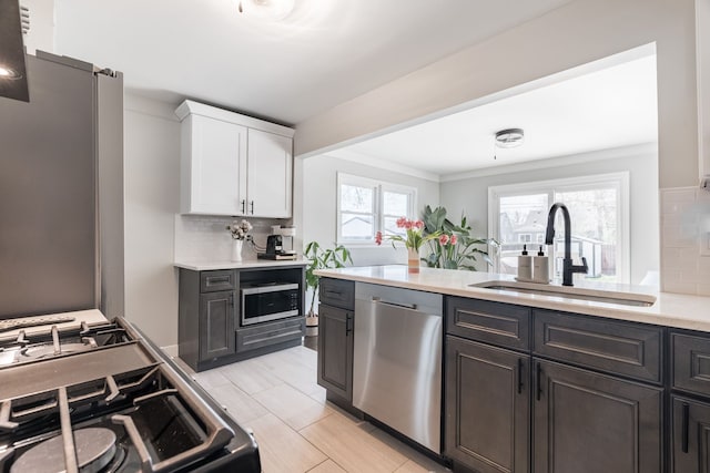 kitchen with white cabinets, appliances with stainless steel finishes, a sink, light countertops, and decorative backsplash
