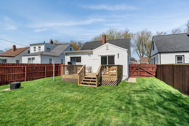 back of property with a wooden deck, a fenced backyard, a chimney, a gate, and a lawn