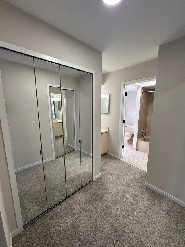 unfurnished bedroom featuring ensuite bathroom, carpet flooring, baseboards, and a closet