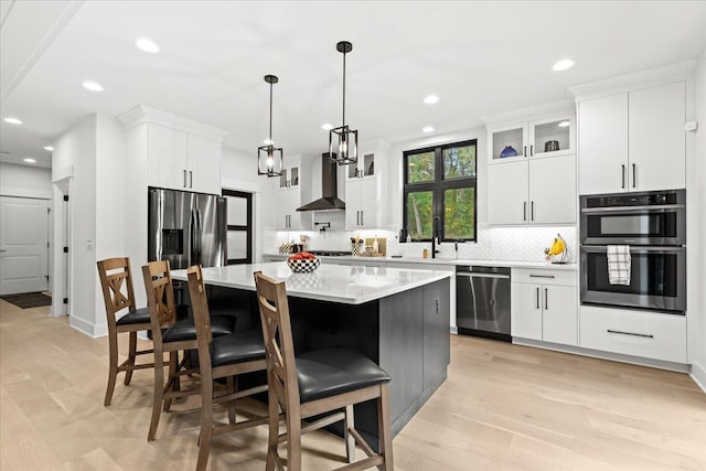 kitchen featuring wall chimney range hood, decorative backsplash, appliances with stainless steel finishes, a sink, and light countertops