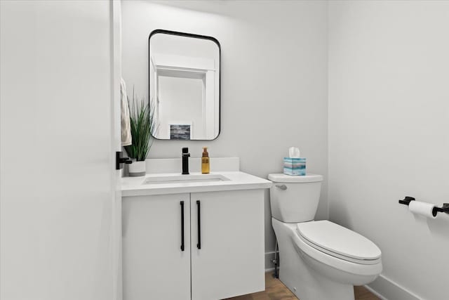 half bath with toilet, baseboards, wood finished floors, and vanity