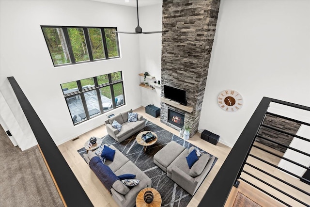 living room with a stone fireplace, baseboards, wood finished floors, a towering ceiling, and visible vents