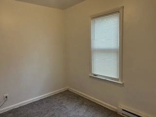 empty room featuring a baseboard heating unit, baseboards, and dark colored carpet