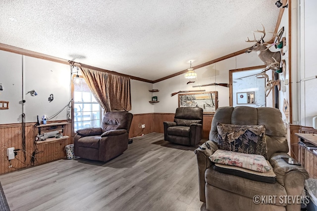 living area with crown molding, wainscoting, a textured ceiling, wood walls, and vaulted ceiling