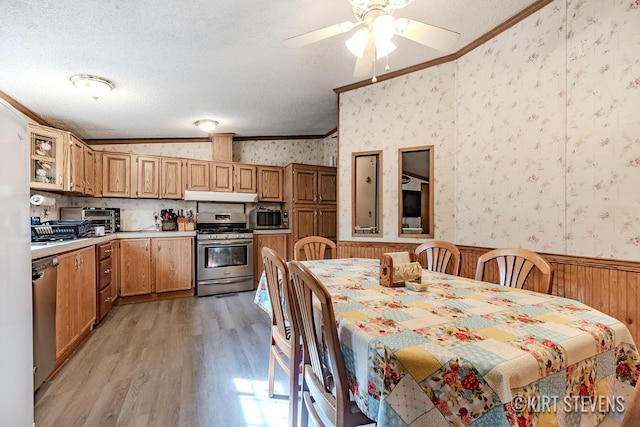 kitchen featuring crown molding, appliances with stainless steel finishes, wainscoting, light wood-type flooring, and wallpapered walls