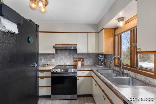 kitchen with a sink, decorative backsplash, under cabinet range hood, stainless steel electric range oven, and freestanding refrigerator