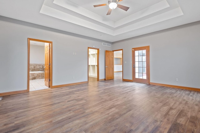 spare room featuring a raised ceiling, visible vents, wood finished floors, and a ceiling fan