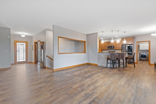 living area with a notable chandelier, wood finished floors, washer / dryer, and baseboards