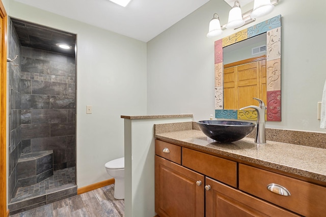 full bathroom with vanity, toilet, a tile shower, visible vents, and wood finished floors