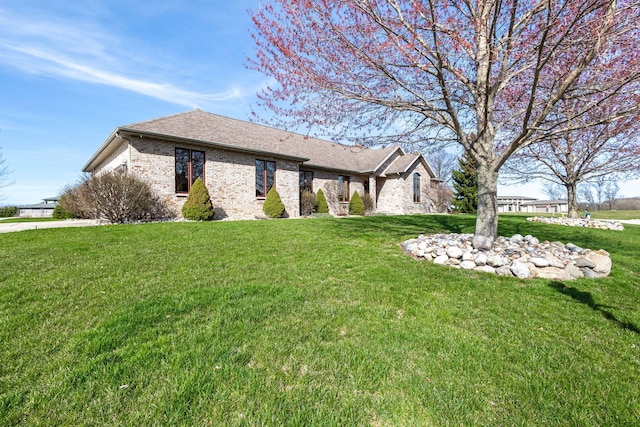 ranch-style house featuring brick siding, a front yard, and roof with shingles