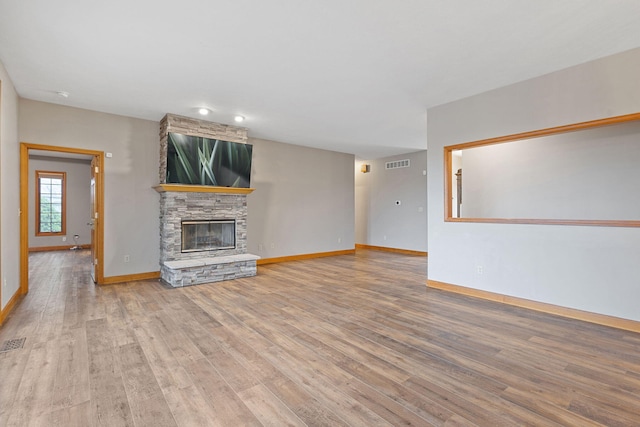 unfurnished living room with wood finished floors, visible vents, a stone fireplace, and baseboards