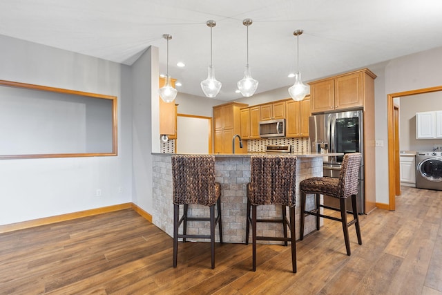 kitchen with a sink, appliances with stainless steel finishes, a breakfast bar, light wood-style floors, and washer / dryer