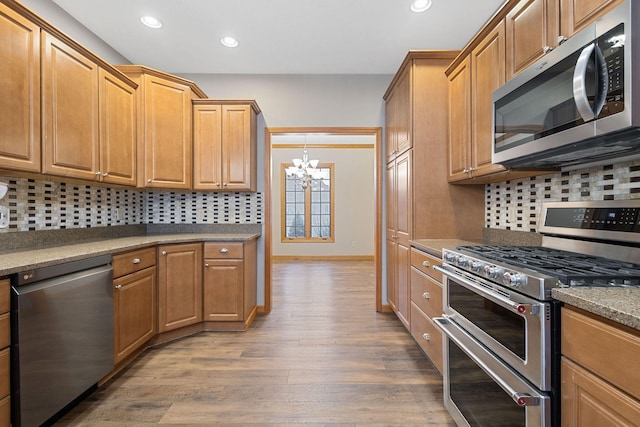 kitchen with an inviting chandelier, wood finished floors, stainless steel appliances, and decorative backsplash