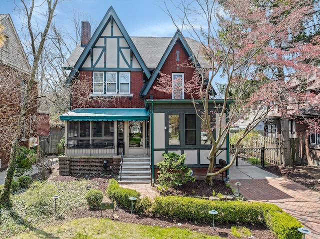 tudor home featuring a chimney, fence, a gate, and a shingled roof