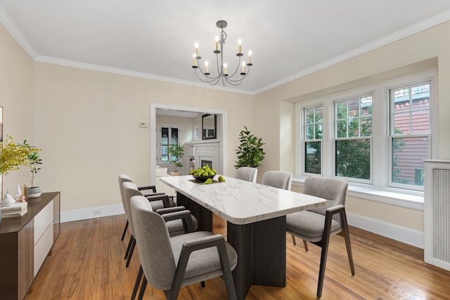 dining space with baseboards, an inviting chandelier, light wood finished floors, ornamental molding, and a fireplace
