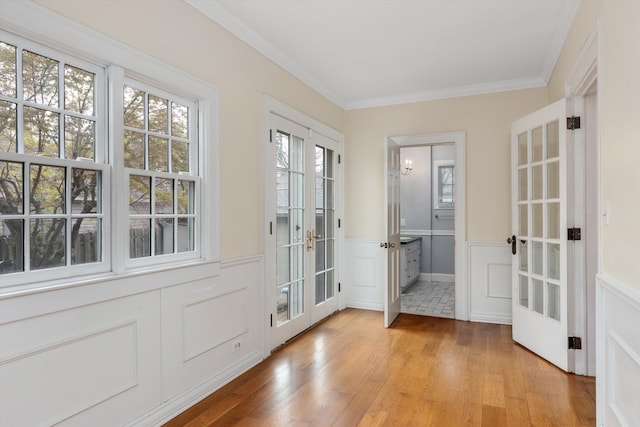 doorway featuring crown molding, light wood-style flooring, french doors, a wainscoted wall, and a decorative wall