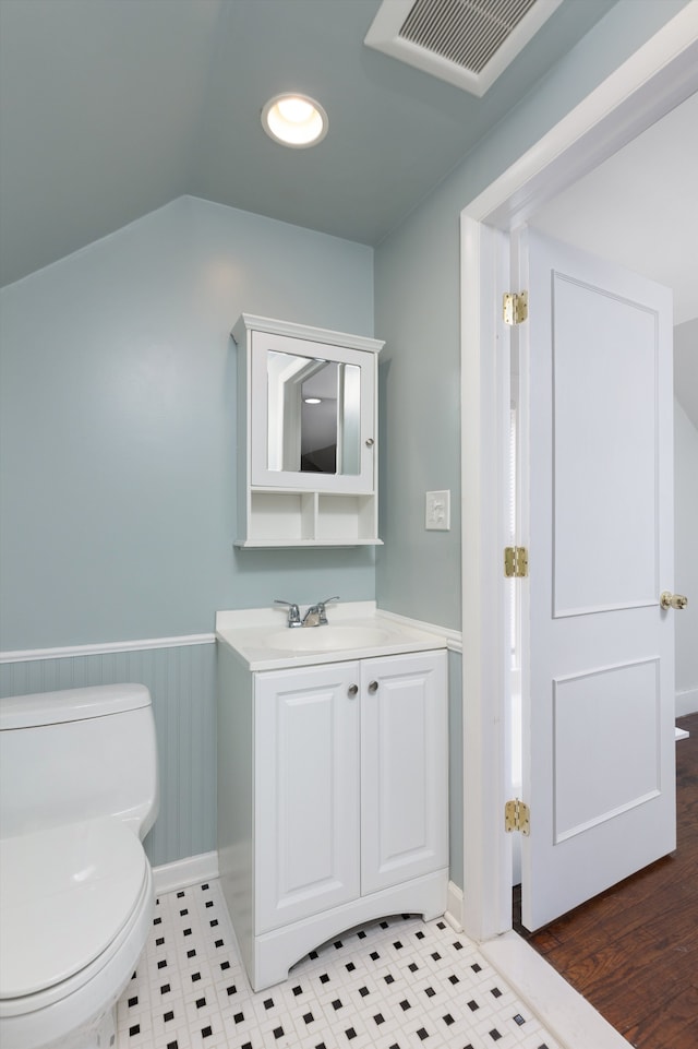 half bathroom featuring toilet, visible vents, wainscoting, and vanity