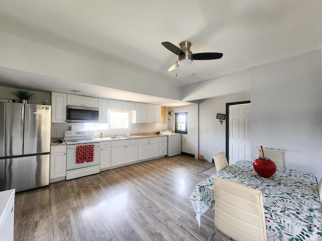 kitchen featuring appliances with stainless steel finishes, a sink, white cabinetry, light wood-type flooring, and washer / clothes dryer