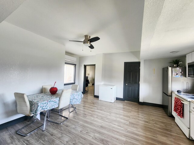 dining room with baseboards, a wall unit AC, a ceiling fan, and light wood-style floors