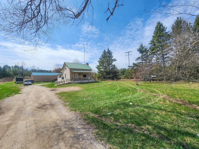 view of front of property with a chimney, a porch, metal roof, dirt driveway, and a front yard