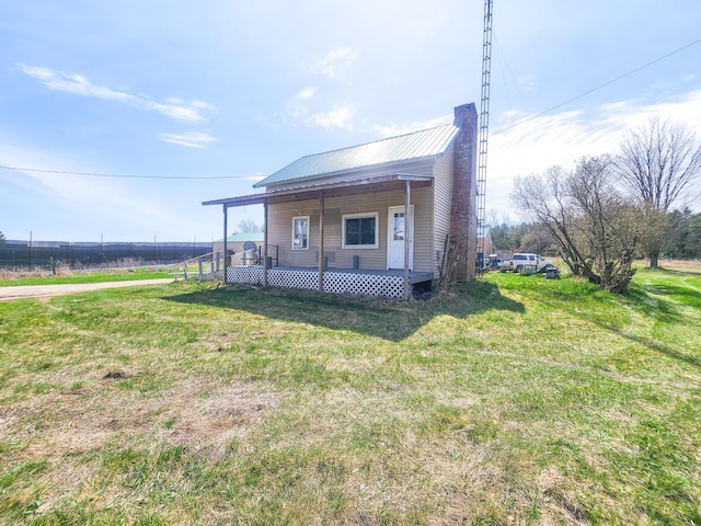 view of front of house featuring a chimney, metal roof, covered porch, a front yard, and fence