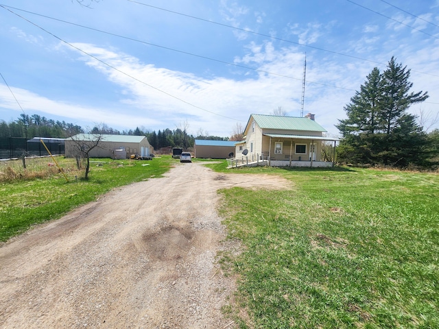 view of front facade with a front yard, metal roof, dirt driveway, covered porch, and a chimney