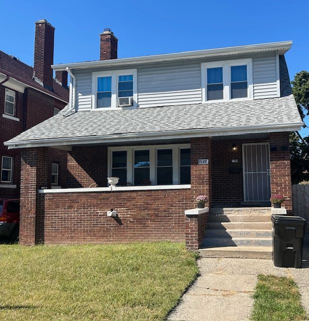 2220 Webb St, Detroit, MI 48206 - view of front of property featuring covered porch, a front yard, brick siding, cooling unit, and a shingled roof