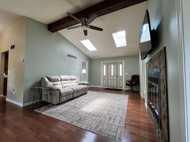 living room with a ceiling fan, a skylight, wood finished floors, beamed ceiling, and a glass covered fireplace