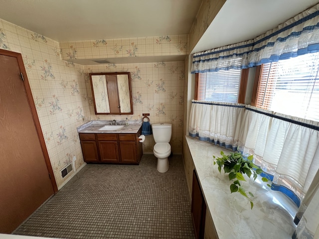 bathroom featuring vanity, toilet, and wallpapered walls