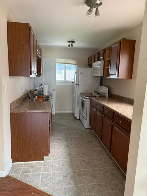 kitchen with white appliances, baseboards, and a sink